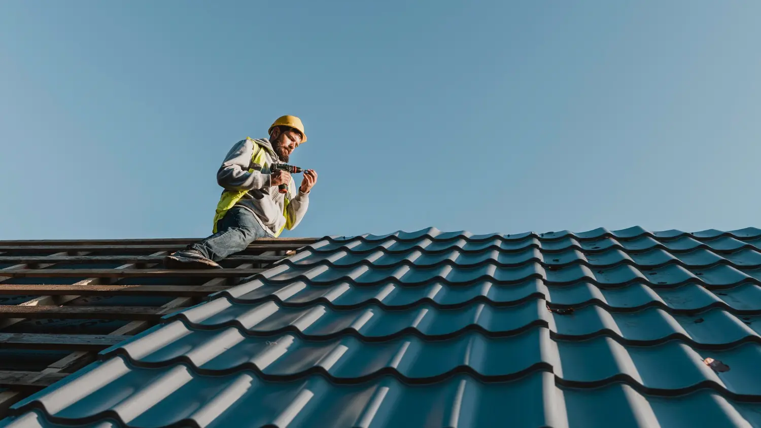 Construction-worker-wearing-a-yellow-hard-hat-and-safety-vest-installing-metal-roofing-sheets